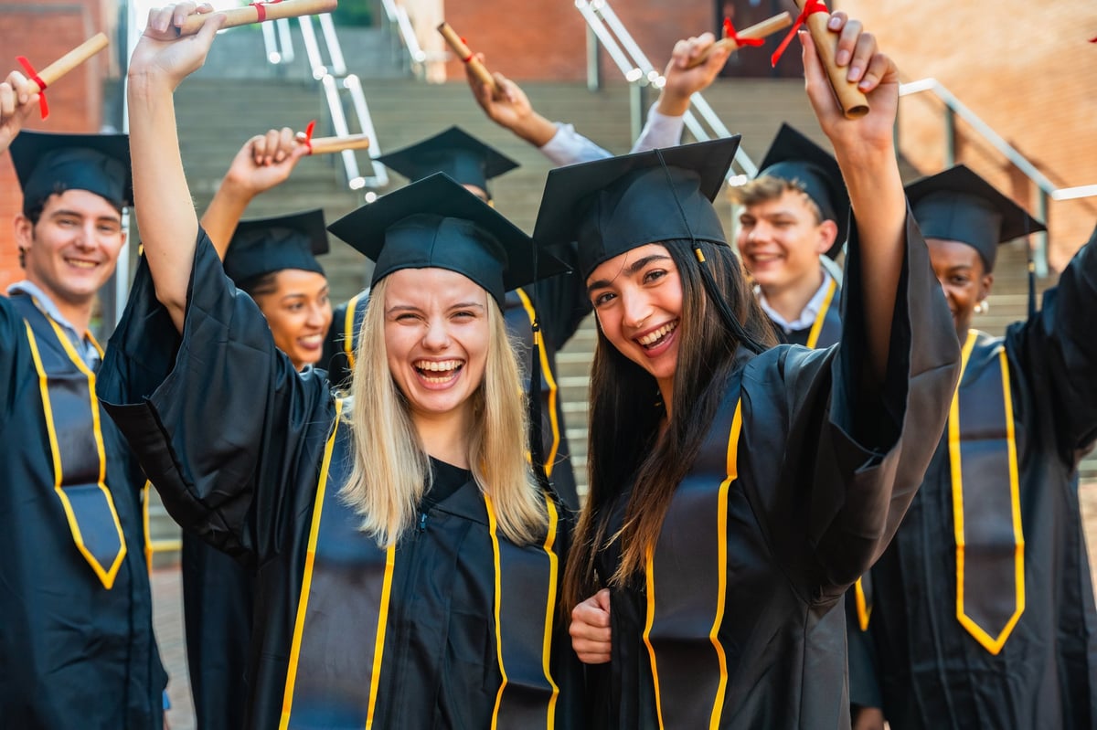 Diverse graduates in caps and gowns holding up their diplomas and celebrating